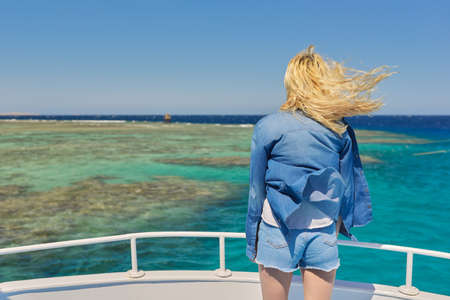 Young blonde female on yacht looking at turquoise coral reefs in Red Seaの写真素材
