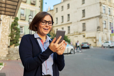 Middle-aged business woman in in cardigan glasses with mobile phoneの写真素材