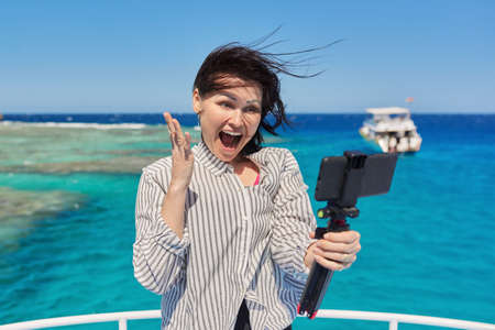 Happy woman recording video stream on smartphone, background is place for diving and snorkelingの写真素材
