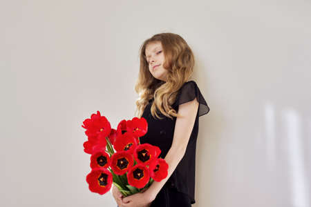 Sad child girl with a bouquet of red tulips in black dressの写真素材