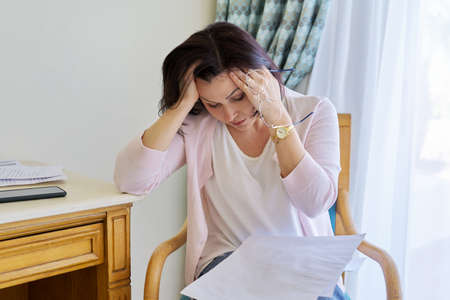 Sad emotion on face of mature woman reading paper letter, contract, document.の写真素材