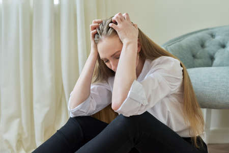 Upset crying young woman sitting at home on the floor.の写真素材