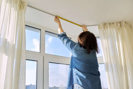 Service for sewing and hanging curtains. Woman with tape measure measuring windowの写真素材