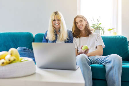 Laughing couple of teenagers having fun, sitting on couch, looking at laptopの写真素材