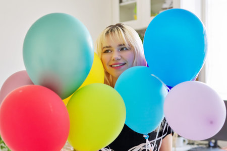 Close up of colored balloons and happy smiling face of blonde teen female