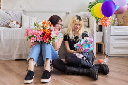 Mom congratulating daughter with bouquet of flowers and surprise gift boxの写真素材