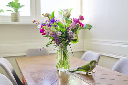 Parrot green pet and bouquet of flowers on the table.の写真素材