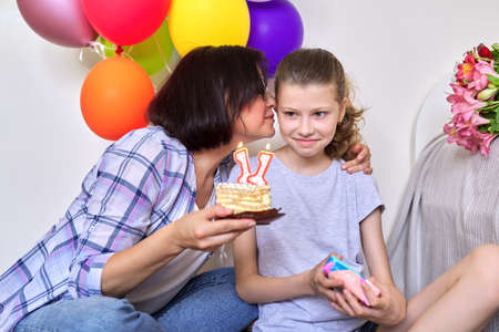 Mom and daughter with birthday cake with candles, gift, balloonsの写真素材