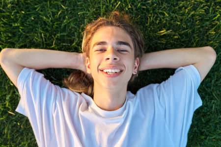 Close-up face of handsome guy 16, 17 years old on green grass, top viewの写真素材