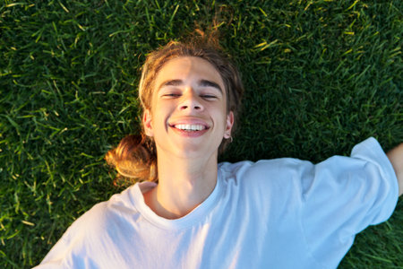 Close-up face of handsome guy 16, 17 years old on green grass, top view