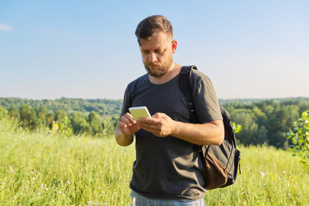 Middle-aged bearded man with backpack using smartphone