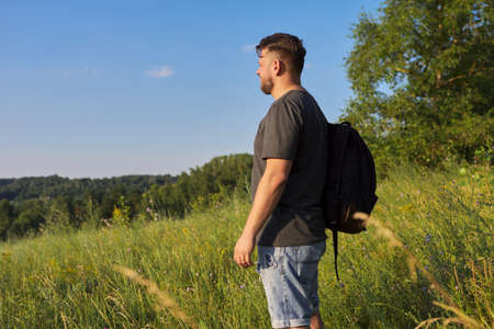 Back view of middle-aged man with backpack looking in distance at natural hillsの写真素材