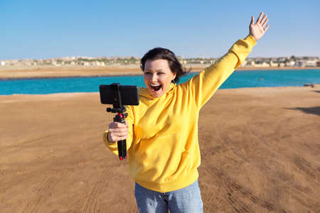 Middle aged woman with smartphone looking at webcam talking recording videoの写真素材