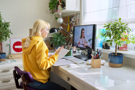 Teenager girl sitting at home studying online using home computer.