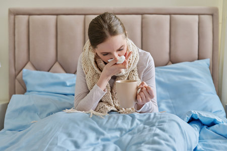 Sick young woman in bed with handkerchief and cup
