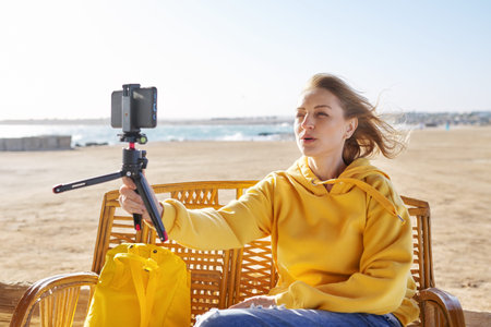 Middle-aged female making online video call talking laughing, sunset seascape background
