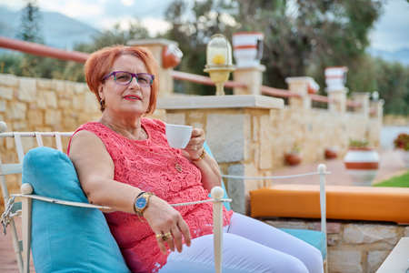 Portrait of beautiful elderly 70s woman relaxing with cup. Smiling senior female with glasses sitting in an outdoor cafe enjoying coffee. Beauty, age, health, pensioner, retired older people conceptの写真素材