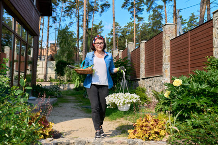 Middle-aged woman in backyard with gardening tools and blooming petunia in pot