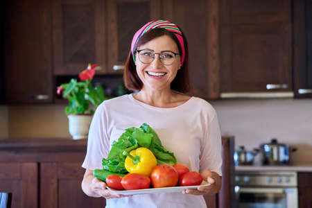 Portrait of an adult woman with a plate of vegetables in the kitchenの写真素材