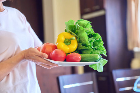 Close-up of a plate with tomatoes, cucumbers, paprika and lettuce in the hands of a woman
