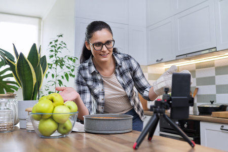 Female recording video of an apple pie recipe on smartphone at home in the kitchenの写真素材