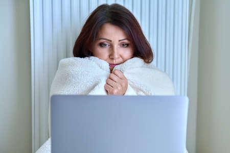 Woman working at home with laptop, warming with blanket and heating radiatorの写真素材