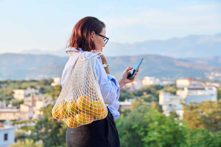Portrait of middle-aged woman with smartphone and trending grid of oranges outdoorsの写真素材