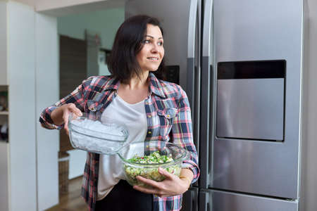 Middle aged woman in the kitchen with salad and a bowl of ice in the kitchenの写真素材