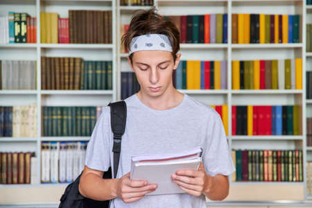 Portrait of a male teenager student looking in a notebook in a library.の写真素材
