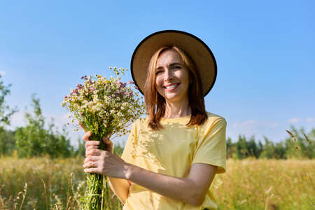 Beautiful happy adult woman with bouquet of wild flowers on summer meadowの写真素材