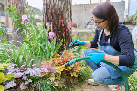 Woman watering plants in a flower bed in the backyard using a hose.