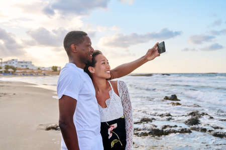Happy couple in love taking selfie together on smartphone, on beachの写真素材