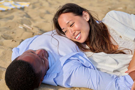 Young happy couple lying on sand, talking enjoying the senses togetherの写真素材