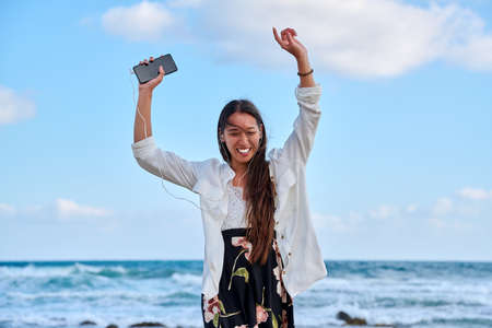 Beautiful woman in headphones with smartphone dancing on the beachの写真素材