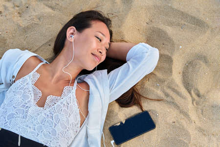 Relaxing young woman in headphones with smartphone on the sand, top viewの写真素材