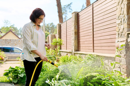 Middle-aged woman watering flowerbeds with a hose