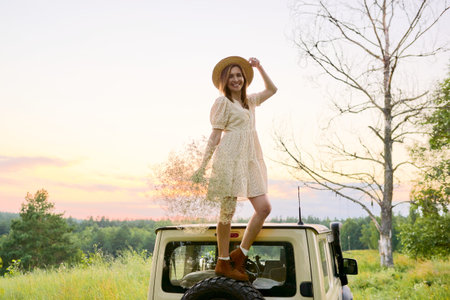Beautiful woman in straw hat dress with bouquet of flowers on the roof of car