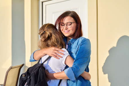 Mom hugging her preteen daughter on the porch of the houseの写真素材