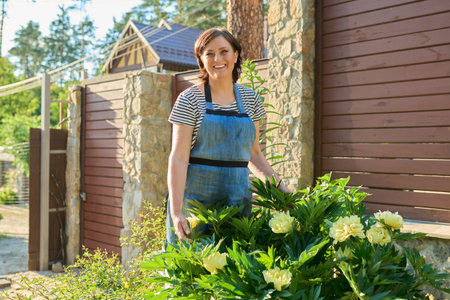 Portrait of middle-aged woman in garden near flowering yellow peony bush