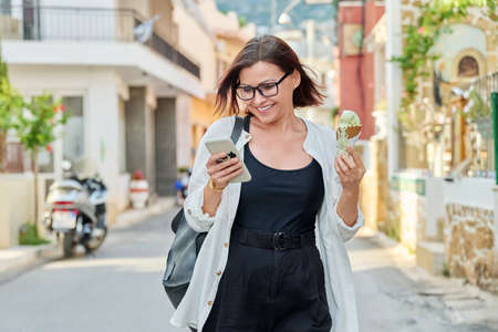 Smiling woman with ice cream walking down the street of summer cityの写真素材