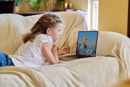 Girl child watching video stream on laptop, resting lying on sofa at home