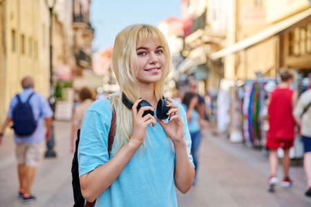 Young woman in headphones with backpack on street of tourist cityの写真素材