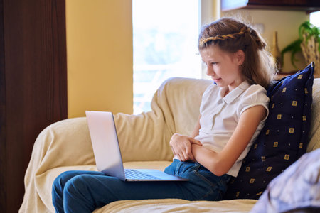 Child girl at home on the sofa with a laptop.