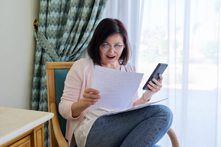 Middle age surprised woman with smartphone business papers sitting at home