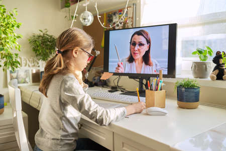 Girl child sitting at home at table with computer listening online lessonの写真素材