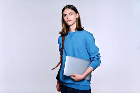 Portrait of serious student guy with backpack laptop looking at camera, light studio backgroundの写真素材