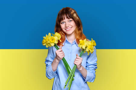 Ukraine flag background, young smiling beautiful woman holding yellow flowersの写真素材