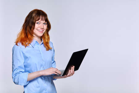 Beautiful teenage female with laptop looking at camera, light studio backgroundの写真素材
