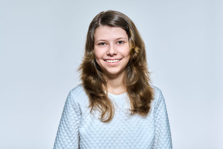 Portrait of schoolgirl 11, 12 years old, girl looking at camera on light studio background