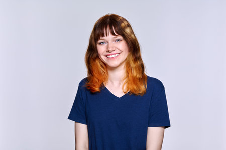 Portrait of young red-haired female looking at camera on light studio background